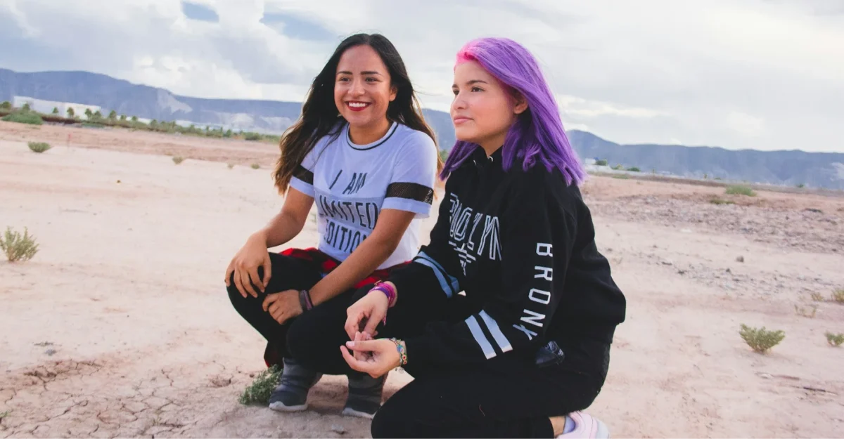 two girls one with purple hair crouched in wide open space