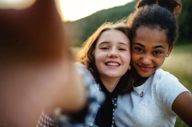 Two teens posing for a selfie outside in low muted warm light
