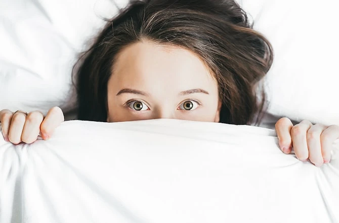 Teen hiding behind white bed duvet