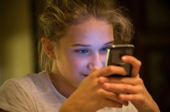 Teen stares into phone with screen light reflecting in her eyes and face