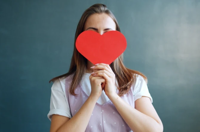 Teenage girl covering face with red heart