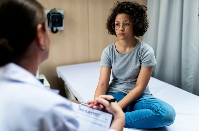 Girl sitting on bed with sad expression listening to doctor
