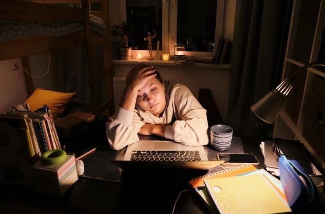 Teen overwhelmed and tired surrounded by books at night in bedroom