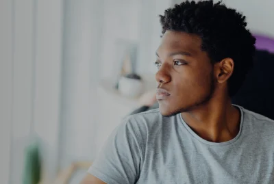 Melancholic headshot portrait of young black man looking aside isolated on blurred indoors background