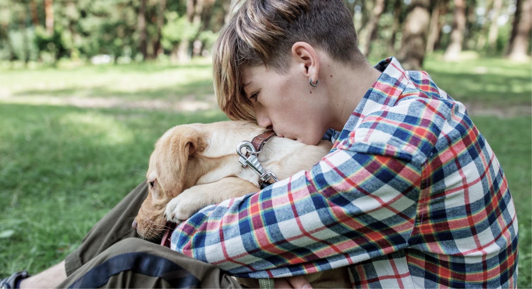 Boy in checkered shirt hugging pet dog in garden for comfort