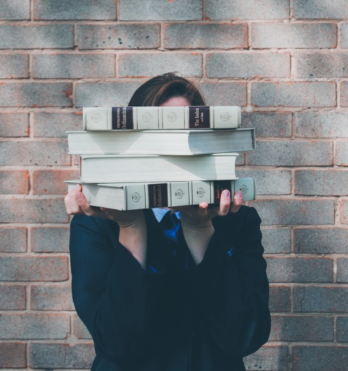 Pupil-hiding-behind-school-books-in-front-of-brick-background