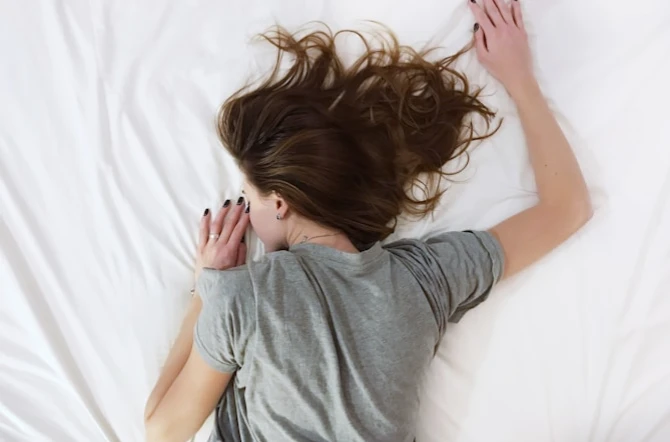 Girl crashed out over bed white sheets with brown hair scattered over shot from above
