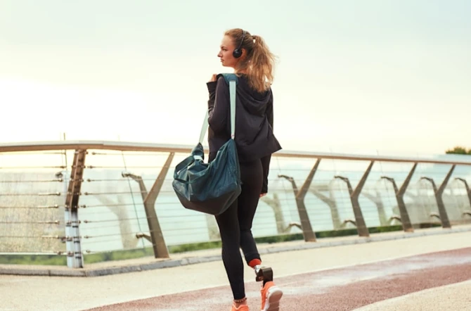 College teen with gym bag and headphones looking out over a modern bridge barrier