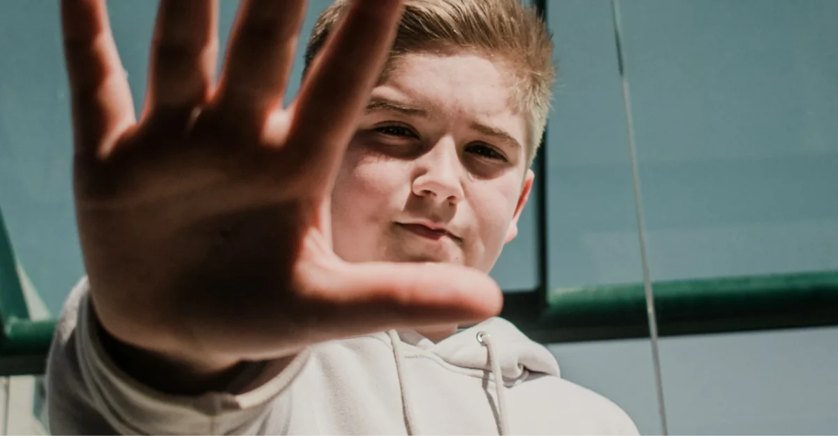 Male teen blocking camera with hand