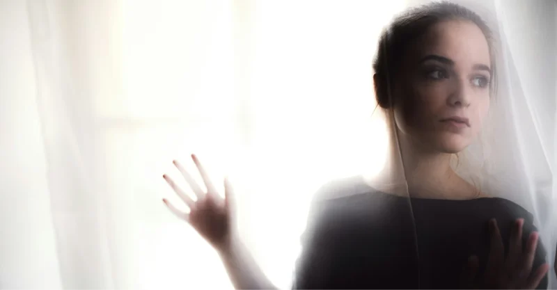 teen girl in shadow looking through mesh curtains