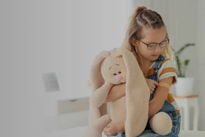 Girl on bed with teddy bear pointing at plaster on her arm