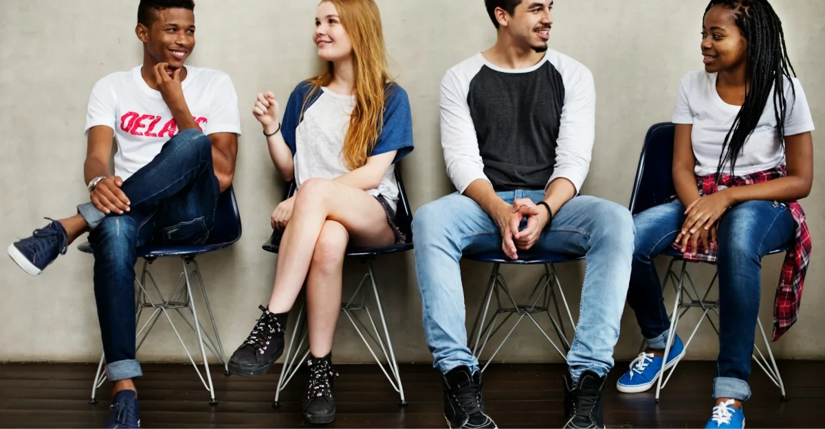 four teens at college sat on bench talking in casual clothes