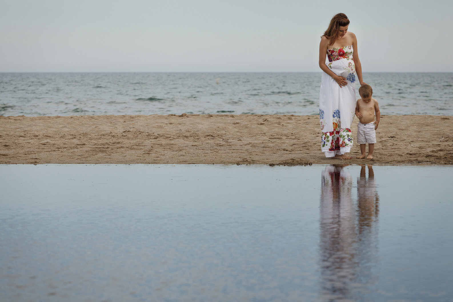 Mother and child at beach touching tummy's