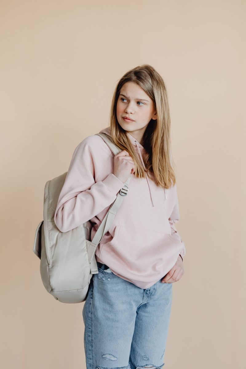 Teen girl in pink sweater and jeans with backpack posing in studio, looking sideways.